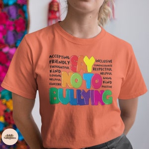 May include: Orange t-shirt with the words "Say No To Bullying" in rainbow colors. The words are surrounded by other positive words like "accepting", "friendly", "inclusive", "compassionate", "respectful", "helpful", "giving", "kind", and "positive".