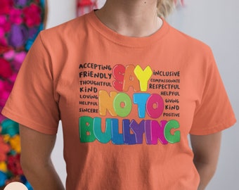 Puede incluir: Camiseta naranja con las palabras "Say No To Bullying" en colores arcoíris. Las palabras están rodeadas de otras palabras positivas como "aceptando", "amigable", "inclusivo", "compasivo", "respetuoso", "servicial", "dando", "amable" y "positivo".