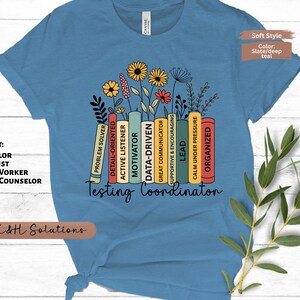 May include: A slate blue t-shirt with a floral design and the words "Testing Coordinator." The design includes colorful books with positive attributes and the text "Custom Text: Counselor, Therapist, Social Worker, School Counselor, Other."