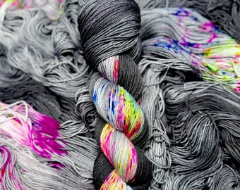 Puede incluir: Un ovillo de hilo gris oscuro con una sección retorcida con colores vibrantes. La sección colorida incluye tonos rosas, amarillos, azules y verdes. El hilo está rodeado por un montón de hilo gris suelto.