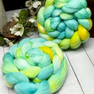 May include: Two balls of hand-dyed yarn in shades of blue, green, and yellow. The yarn is arranged in a braided pattern.
