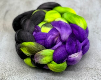May include: A braided bundle of yarn in black, green, and purple shades. The yarn is arranged in a heart shape.