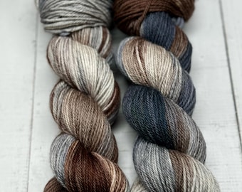 Puede incluir: Dos ovillos de hilo, uno marrón y gris con rayas blancas, y otro azul y gris con rayas blancas.