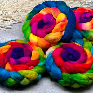 Può includere: Quattro trecce circolari di lana cardata multicolore con un vibrante gradiente di fibre blu, verdi, gialle, arancioni, rosse e viola. Ogni bobina spessa e morbida è avvolta strettamente in una forma rotonda, mostrando uno spettro di colori.
