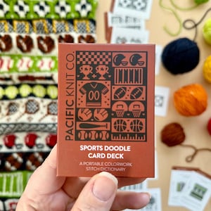 May include: A brown card with a white border and the text "PACIFIC KNIT CO." in white. The card features a variety of sports-themed illustrations in black and white, including a football, basketball, baseball bat, and a trophy. The text "SPORTS DOODLE CARD DECK" is printed in white on a black background. The text "A PORTABLE COLORWORK STITCH DICTIONARY" is printed in white on a black background.