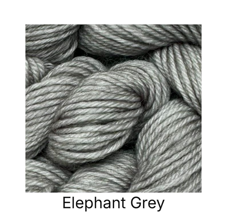 May include: Close-up of gray yarn skeins. The yarn is a light, solid gray color, with a thick, textured appearance. The text "Elephant Grey" is displayed at the bottom of the image. This yarn is suitable for various knitting and crochet projects.