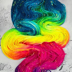 May include: A colourful skein of yarn, displaying a gradient from deep blue to bright green, yellow, orange, and then a rich pink and purple. The yarn has a speckled texture, adding visual interest.