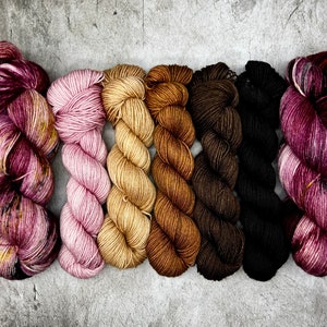 Könnte beinhalten: Sechs Wollknäuel in verschiedenen Farben, von Rosa über Beige bis Braun und Schwarz, nebeneinander angeordnet. Die Farben umfassen Rosatöne, Beige, Braun und Schwarz. Ideal für Strick- oder Häkelprojekte.