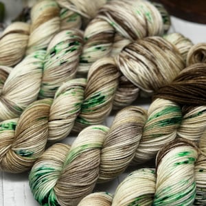 May include: A skein of yarn in shades of brown, cream, and green. The yarn is hand-dyed and has a variegated color pattern.