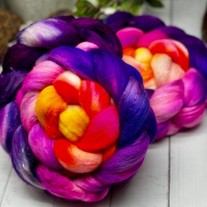 May include: A colorful, braided ball of yarn in shades of purple, pink, orange, and yellow. The yarn is arranged in a flower-like pattern.