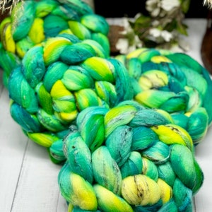 May include: Three skeins of hand-dyed yarn in shades of green, yellow, and blue. The yarn is braided and has a speckled appearance.