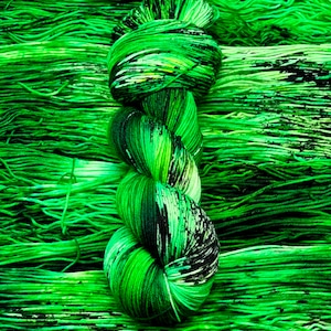 Könnte beinhalten: Ein Knäuel grüner und schwarzer Wolle mit einem gesprenkelten Muster. Die Wolle ist zu einem Knoten gedreht und liegt auf einem Hintergrund aus ähnlicher Wolle.