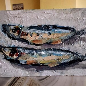 May include: Oil painting of two fish, rendered with thick brushstrokes. The fish are primarily blue, with accents of orange, brown, and white. The background is a textured, light gray. The artwork has a rustic, impressionistic style.