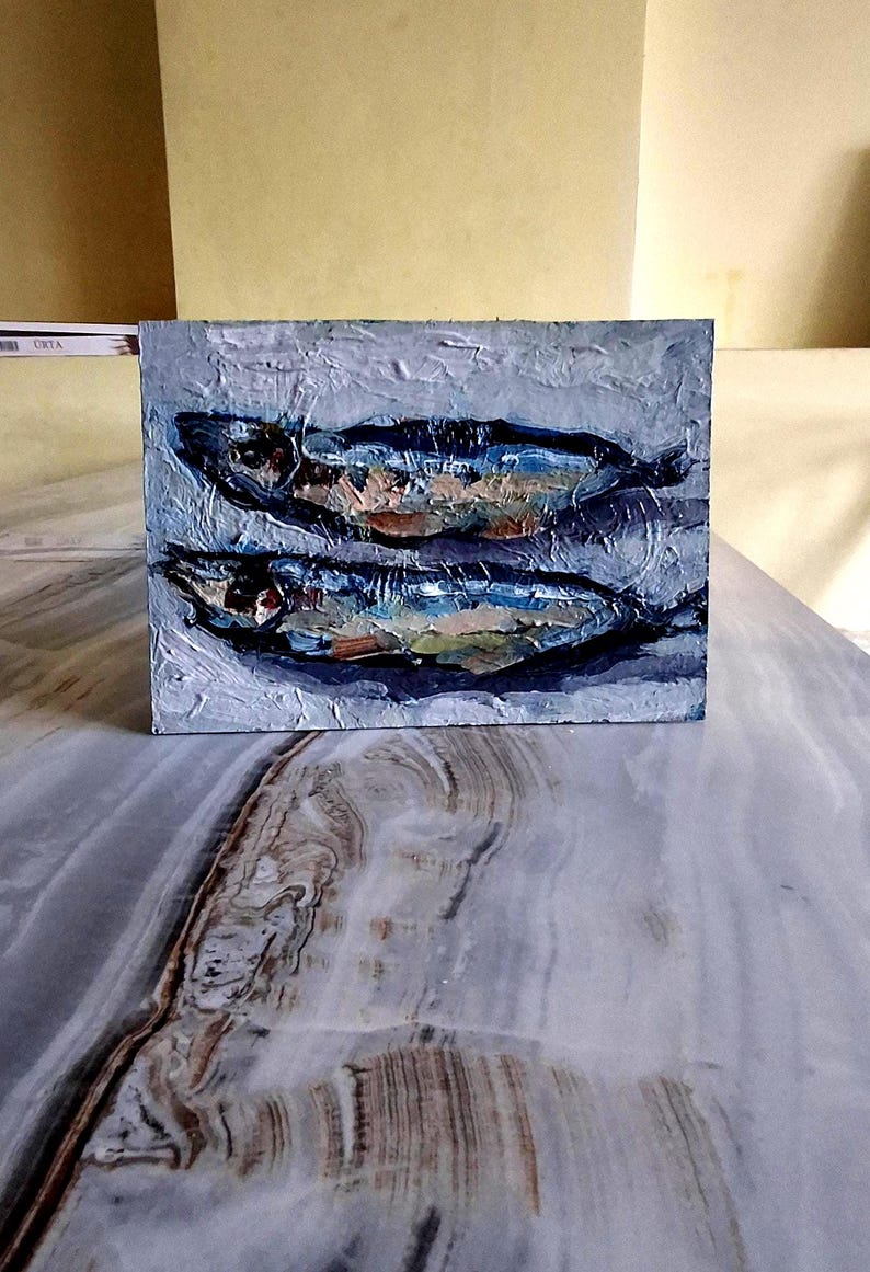 May include: An oil painting on a square canvas depicts two fish in shades of blue, brown, and white. The textured brushstrokes create a sense of depth and movement. The artwork is set against a light gray background.