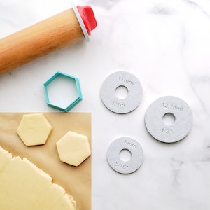 May include: A close-up of a baking scene with a rolling pin, cookie cutters, and dough. There are three round metal measuring guides with the text "11mm 7/16", "12.7mm 1/2", and "8mm 5/16".