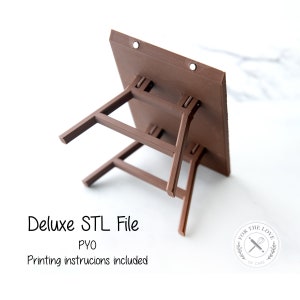 Puede incluir: Una mesa plegable de color marrón, impresa en 3D, con una superficie plana y cuatro patas. La mesa está diseñada para ser utilizada como un soporte para pasteles. El texto "Deluxe STL File PYO Printing instructions included" es visible debajo de la mesa.