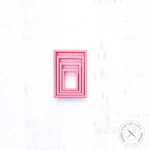 May include: Four pink nesting rectangular cookie cutters on a white background.