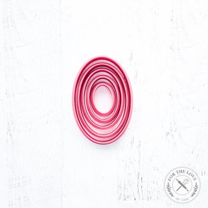 May include: Set of six red oval cookie cutters, nested together in decreasing size. The cutters are made of metal and have a smooth, shiny finish.