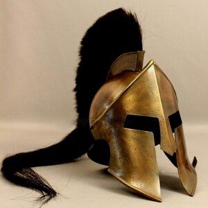 May include: A bronze-colored Spartan helmet with a black plume. The helmet has a classic design with cheek guards and eye openings. The plume is long and flowing, adding to the helmet's historical appearance.