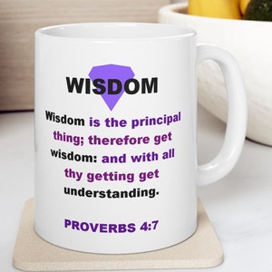 May include: White ceramic mug with the word "WISDOM" above a purple diamond shape. The mug features a quote from Proverbs 4:7 in black and purple text. The mug sits on a beige coaster.