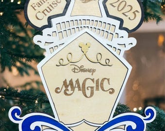 May include: Wooden Christmas ornament with the text "Family Cruise 2025" and "Disney MAGIC". The ornament has a ship design with blue and white accents. It is hanging on a Christmas tree.