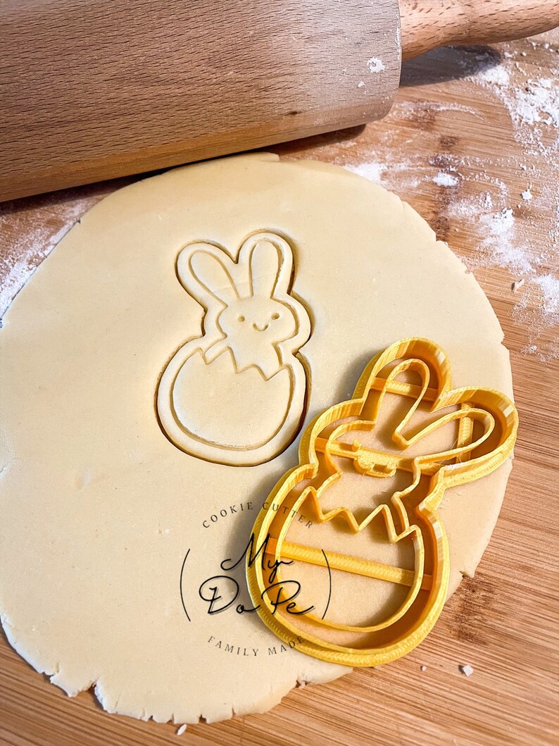Pu&ograve; includere: Tagliapasta in plastica gialla a forma di coniglio che esce da un uovo. Il tagliapasta &egrave; sopra un foglio di pasta per biscotti non cotta. Il tagliapasta ha il testo "My Do Pe" e "Cookie Cutter Family Made".
