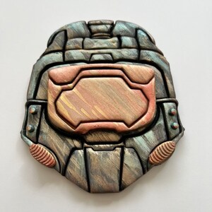 May include: A metallic-looking, decorative helmet, possibly a cosplay prop or art piece. The helmet is primarily gray with bronze and copper accents. The design features a visor and other details, suggesting a futuristic or sci-fi theme.