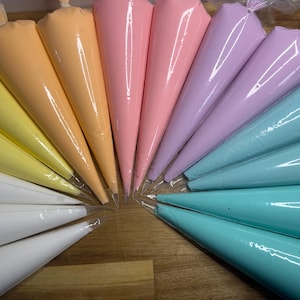 May include: A collection of piping bags filled with colorful frosting in a rainbow of pastel shades. The colors include yellow, orange, pink, purple, and teal. The bags are arranged in a semi-circle on a wooden surface, ready for decorating.