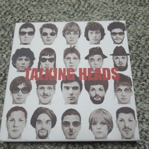 Op de afbeelding: Een zwart-wit fotocollage van de band Talking Heads. De bandleden zijn gerangschikt in een rasterpatroon met de bandnaam in rode letters bovenaan.