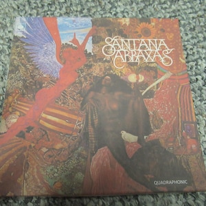 May include: Album cover for Santana's Abraxas. The artwork features a vibrant, colorful illustration with figures, musical instruments, and floral elements. The album title is prominently displayed. The word "QUADRAPHONIC" is at the bottom.