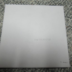 Könnte beinhalten: Weißes Vinyl-Schallplattencover mit dem Text "The Beatles" in der Mitte.