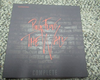 May include: A square, dark gray album cover with the words "Pink Floyd The Wall" in coral script. The background features a brick wall design. The word "COMPLETE" is at the bottom, and "QUADRAPHONIC" is at the top.