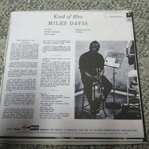 K&ouml;nnte beinhalten: Ein Schwarzwei&szlig;foto eines Mannes, der Trompete spielt. Das Foto stammt von der R&uuml;ckseite einer Schallplatte mit dem Titel "Kind of Blue" von Miles Davis. Der Text "CRI" ist auf einem Notenst&auml;nder im Hintergrund zu sehen.
