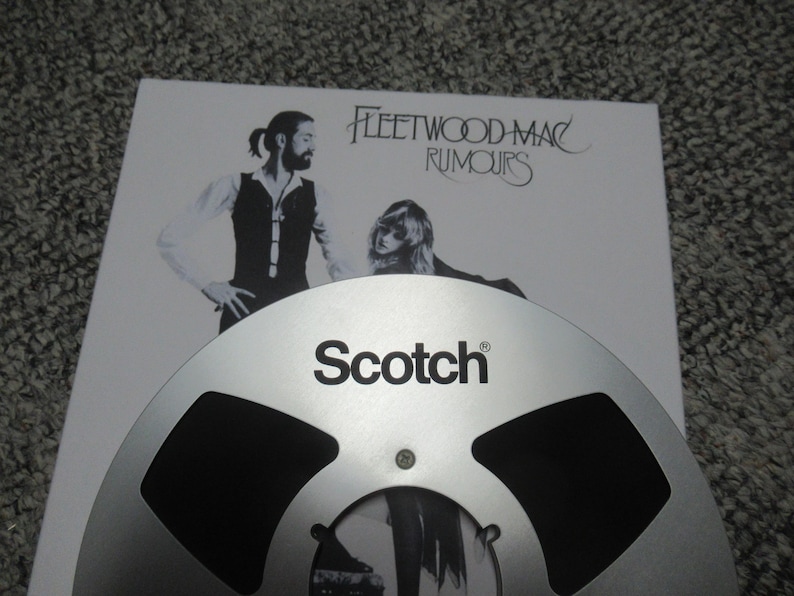Puede incluir: Una cinta de carrete a carrete plateada con la palabra "Scotch" impresa en ella. La cinta est&aacute; encima de una portada de &aacute;lbum blanca con el texto "Fleetwood Mac Rumours".
