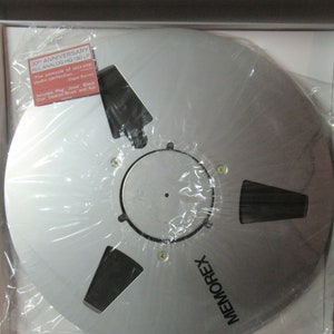 Puede incluir: Una cinta de carrete a carrete Memorex plateada en una caja blanca, envuelta en pl&aacute;stico transparente. La cinta tiene un cubo central con recortes y est&aacute; etiquetada como "30th Anniversary All Analog HQ 180 LP". Una peque&ntilde;a etiqueta enumera las canciones incluidas.