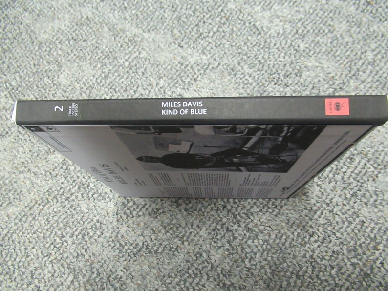 K&ouml;nnte beinhalten: Schwarze Box mit dem Text "MILES DAVIS KIND OF BLUE" auf dem R&uuml;cken. Die Nummer "2" befindet sich auf der linken Seite des R&uuml;ckens. Die Box steht auf einem grauen Teppich.