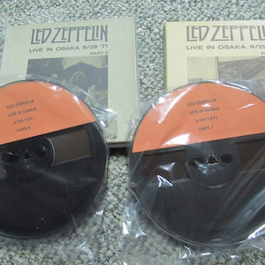 May include: Two black audio cassette reels with orange labels. The labels read "LED ZEPPELIN LIVE IN OSAKA 9/29/1971" and "TAPE 1" and "TAPE 2". The reels are packaged in clear plastic bags.