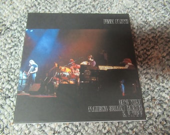 May include: A black and white album cover for Pink Floyd's "The Wall" album. The cover features a black and white photo of the band performing on stage. The album title is printed in white on the cover.