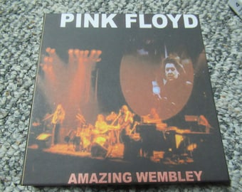 May include: A black and white album cover with the text "PINK FLOYD" in white letters. The album cover features a photo of a concert with a band performing on stage. The text "AMAZING WEMBLEY" is at the bottom of the cover.