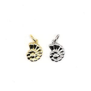 May include: Two small, seashell-shaped pendants. One is gold-coloured, the other is silver-coloured. Both have a loop at the top for attaching to a chain or bracelet. The pendants are set against a white background.