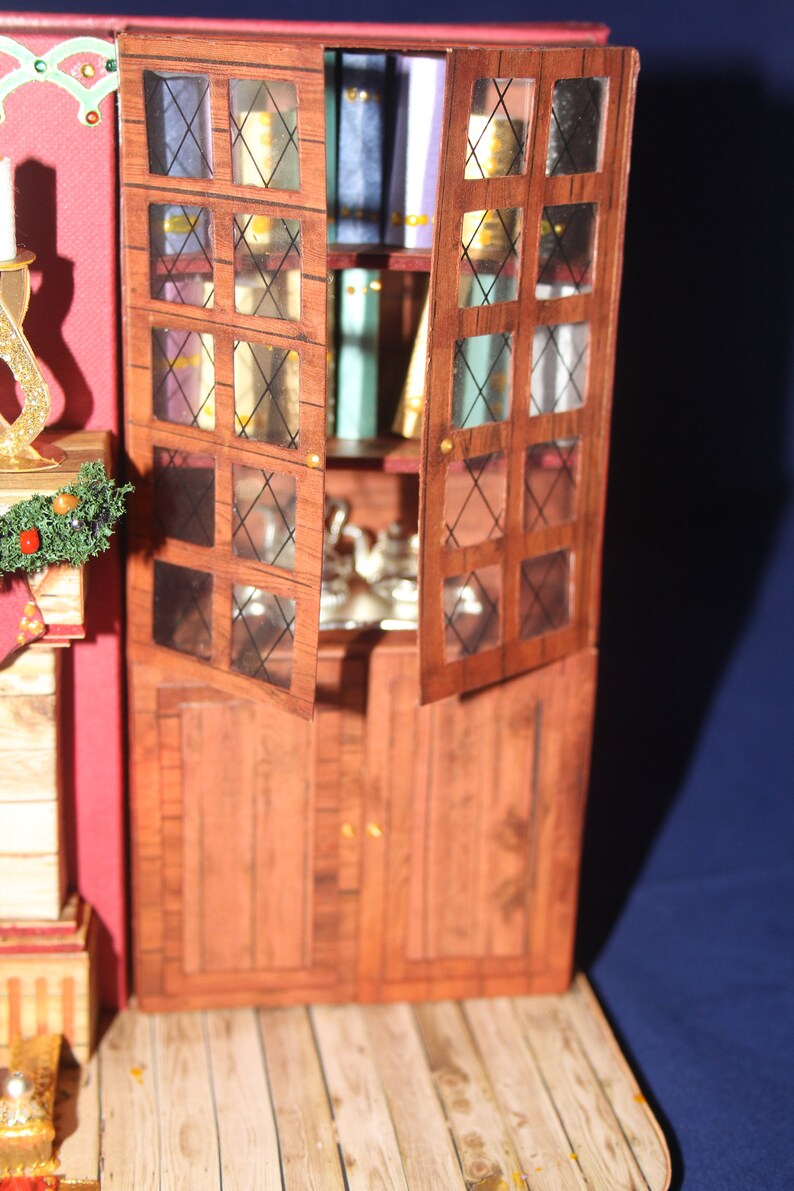 May include: A wooden cabinet with glass doors and shelves. The cabinet is painted a dark brown color and has a distressed finish. The glass doors have a diamond pattern and are open, revealing shelves filled with books and other items. The cabinet is sitting on a wooden floor.