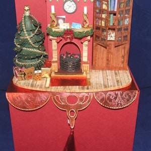 May include: A red and gold Christmas card with a pop-up scene of a fireplace, a Christmas tree, and a bookcase. The fireplace has a glowing fire and a mantle with candles and decorations. The Christmas tree is decorated with gold ornaments and lights. The bookcase is filled with books and has a small decorative bird on top.