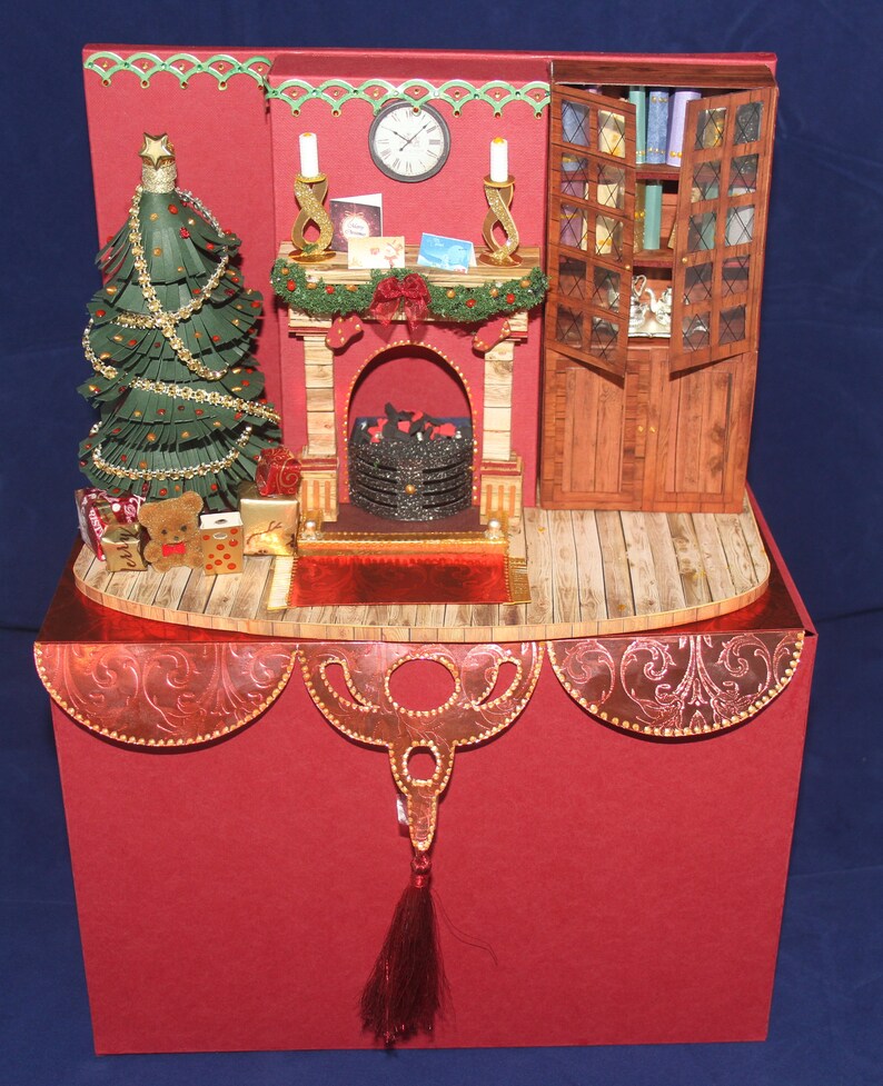 May include: A red and gold Christmas card with a pop-up scene of a fireplace, a Christmas tree, and a bookcase. The fireplace has a glowing fire and a mantle with candles and decorations. The Christmas tree is decorated with gold ornaments and lights. The bookcase is filled with books and has a small decorative bird on top.
