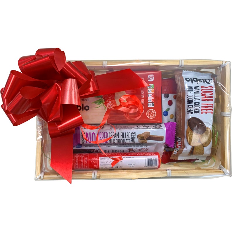 May include: A gift basket filled with various chocolate and cookie snacks. The basket is wrapped in clear cellophane and tied with a red bow. The snacks include a sugar-free vanilla cookie with cocoa cream, a chocolate wafer, and a milk chocolate bar.