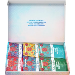 May include: A gift box filled with six Epsom bath salt sachets, each with a different floral design and label, such as "Calm & Soothe" and "Breathe Easy." The box also features text stating "Premium Epsom Salt" and its benefits.