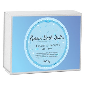 May include: A white gift box with a blue background and a circle containing the text "Epsom Bath Salts 6 Scented Sachets Gift Box 100% Pure Natural Salts. Premium quality Magnesium Sulphate. Relax & revive tired & aching muscles with our mineral rich salts. 6x35g"