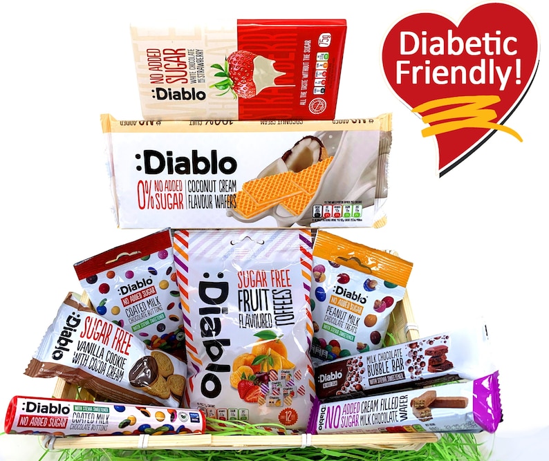 May include: A wooden basket filled with various sugar-free snacks, including chocolate wafers, fruit flavored candies, peanut milk chocolate, and chocolate cookie wafers. The basket is decorated with green grass and a red heart with the text "Diabetic Friendly!"