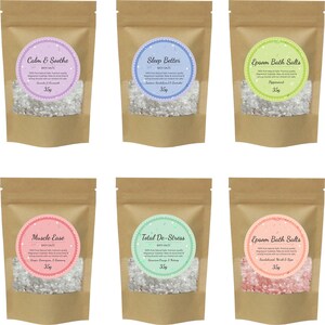 May include: Six brown paper pouches with white bath salts inside. Each pouch has a round label with a different color and scent. The labels read: Calm & Soothe, Sleep Better, Epsom Bath Salts, Muscle Ease, Total De-Stress, and Epsom Bath Salts. Each pouch contains 35g of bath salts.
