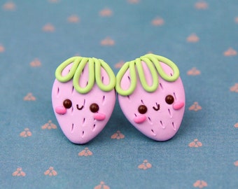 May include: A pair of pink and green clay earrings shaped like strawberries with happy faces.