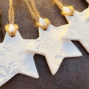 May include: Five white star-shaped decorations with a snowflake design, each with a twine loop for hanging.